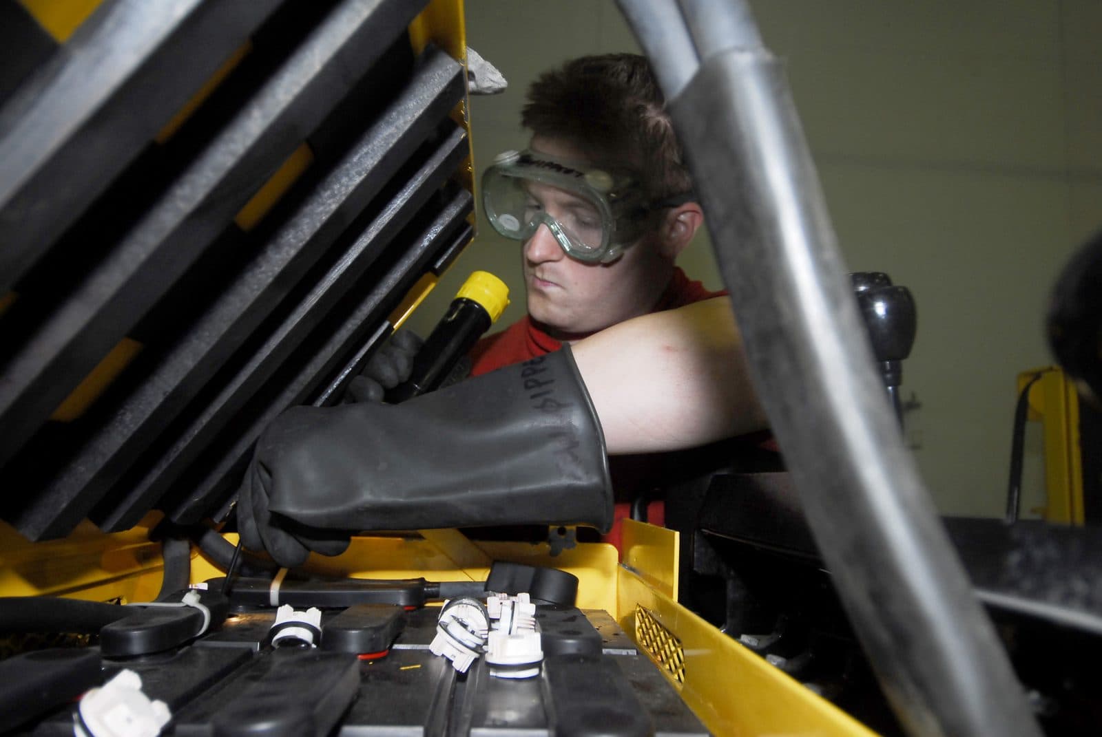 Forklift technician wearing safety goggles and an acid-resistant glove testing cells and connections on a newly installed electric forklift battery before the first charge cycle.